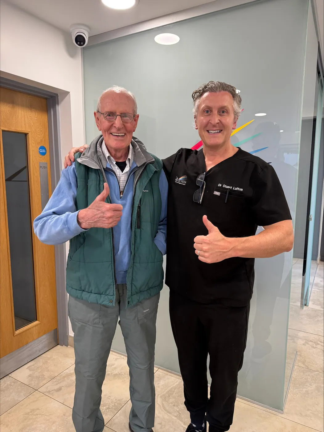 Dr Stuart Lutton standing with a smiling patient in a New Life Teeth clinic, both giving a thumbs up